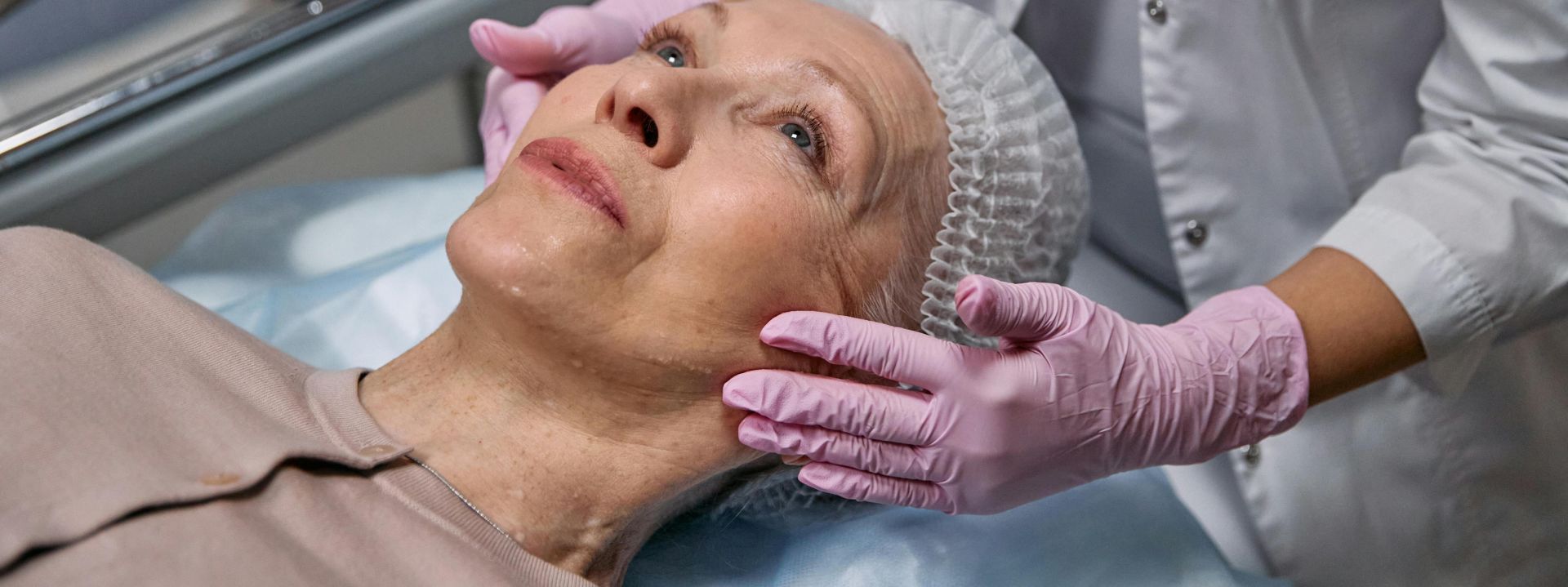 A mature woman in a spa receiving a relaxing facial treatment from a professional in a medical clinic setting.